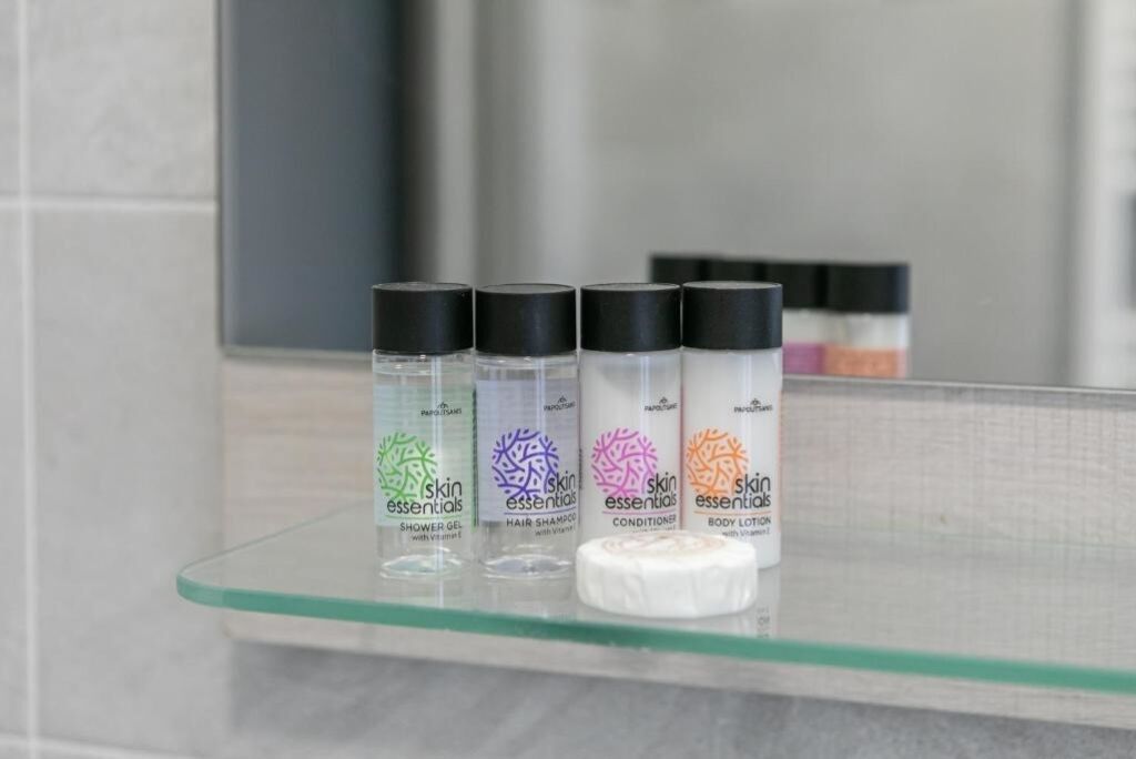 Four bottles of skin essentials on a glass shelf in a bathroom.