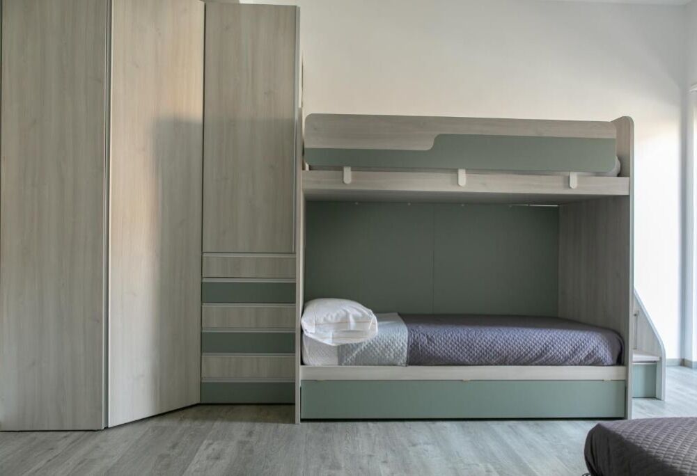 A bunk bed with a built-in wardrobe, a small bedside table, and a window with natural light.