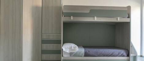 A bunk bed with a built-in wardrobe, a small bedside table, and a window with natural light.