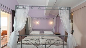 Ein Himmelsbett mit weißen Vorhängen, einem Metallgestell und einer gemusterten Bettdecke.