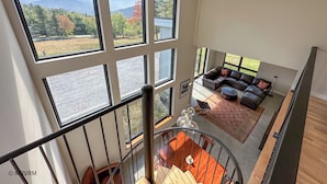 Un vaste espace de vie agrémenté d’une grande fenêtre donnant sur un paysage pittoresque, d’un escalier moderne et d’un coin salon confortable.