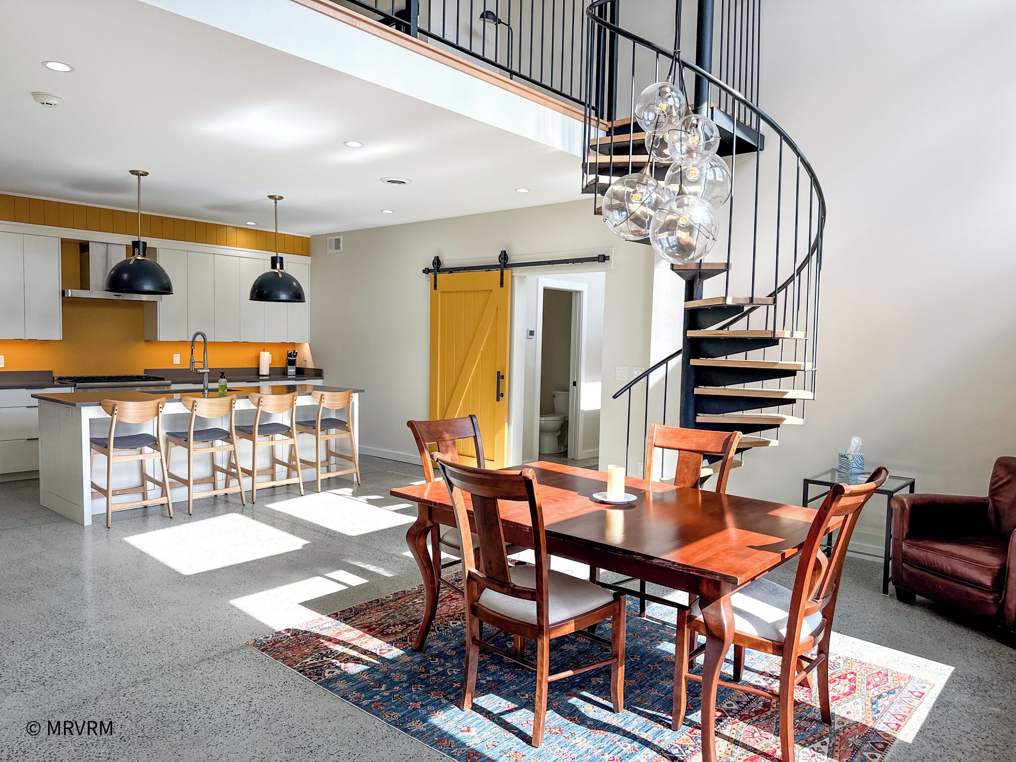 Une cuisine moderne dotée d’un îlot central, d’un coin repas avec une table et des chaises en bois, et d’un escalier en colimaçon.