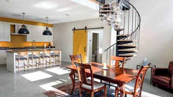 Une cuisine moderne dotée d’un îlot central, d’un coin repas avec une table et des chaises en bois, et d’un escalier en colimaçon.