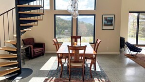 Un intérieur moderne agrémenté d’un escalier en colimaçon, de grandes fenêtres offrant une vue sur les montagnes, un coin repas avec une table et des chaises, et un espace salon confortable avec un canapé en cuir.