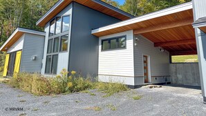 Une maison moderne à deux étages, avec une façade grise et blanche, de grandes fenêtres et un toit en bois.