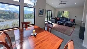 Un vaste espace de vie comprenant une grande table à manger en bois, un canapé en cuir noir et un ventilateur de plafond.