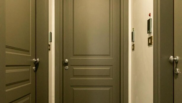 Un couloir avec trois portes, chacune équipée d’une sonnette et d’un interrupteur.