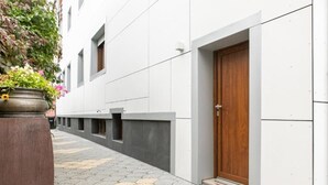 Un étroit sentier mène à un bâtiment doté d’une porte en bois et orné d’une plante en pot, elle-même fleurie.