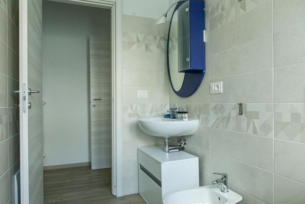 A modern bathroom with a white sink, a mirror, and a shower area.