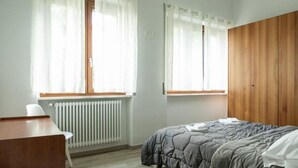 Una camera da letto con un letto, una scrivania e una sedia. Sono presenti due finestre con tende.