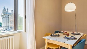 Un coin repas avec une table dressée pour quatre personnes, un lampadaire et une fenêtre donnant sur un immeuble.