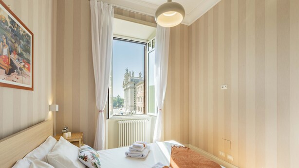 Une chambre d’hôtel avec un grand lit, une vue sur un immeuble par la fenêtre et une petite table avec une lampe.