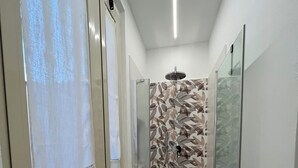 Un pasillo estrecho con cabina de ducha de vidrio, una ventana con persianas y una pared con diseño de hojas.