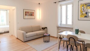 Una sala de estar moderna con un sofá, una mesa de comedor con sillas, una mesita auxiliar y un cuadro en la pared.