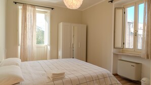 Un dormitorio con cama, armario, radiador y ventana con cortinas.