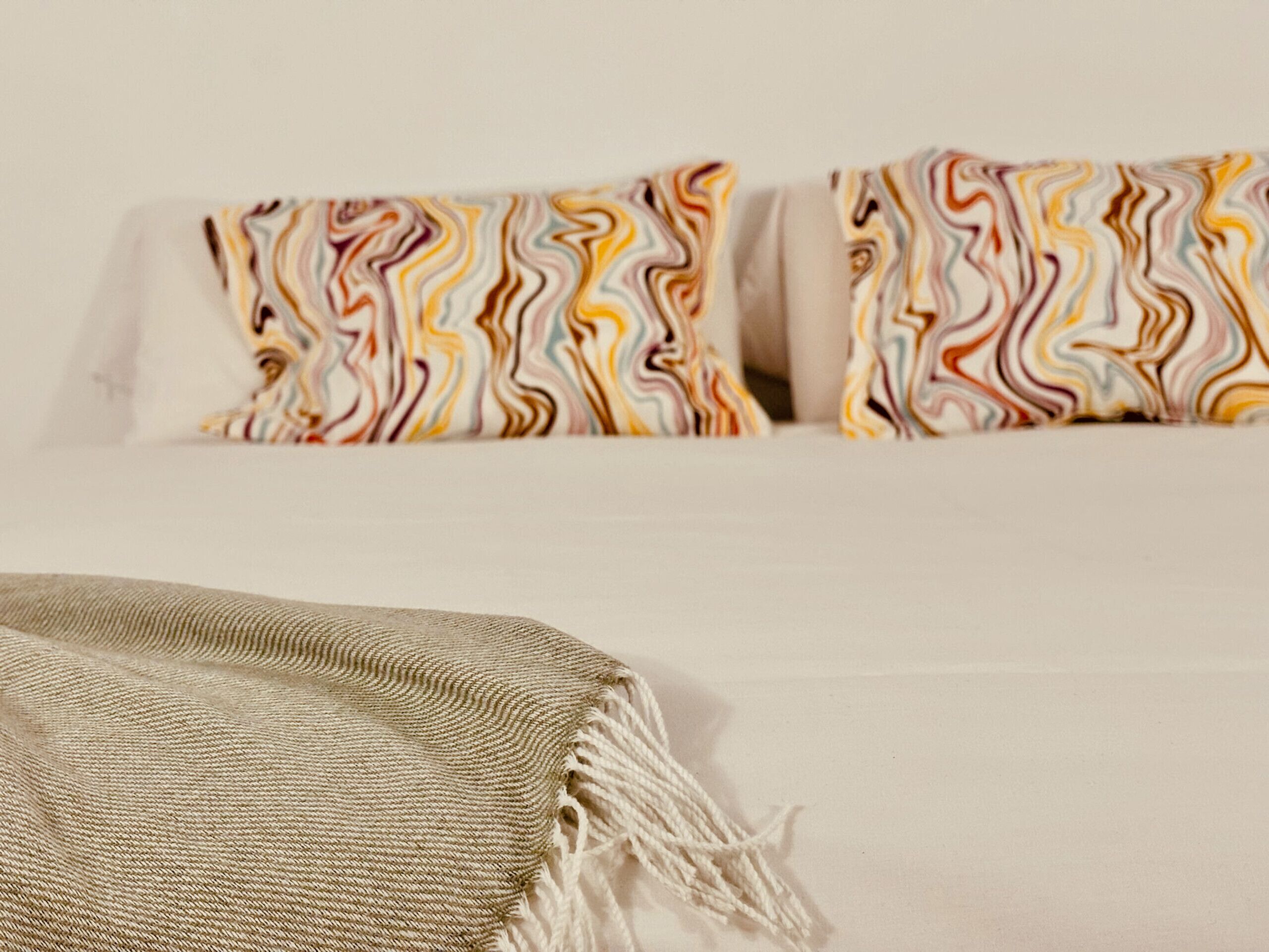 Un canapé blanc agrémenté de coussins aux motifs colorés et ondulés, ainsi que d’un plaid à texture intéressante.