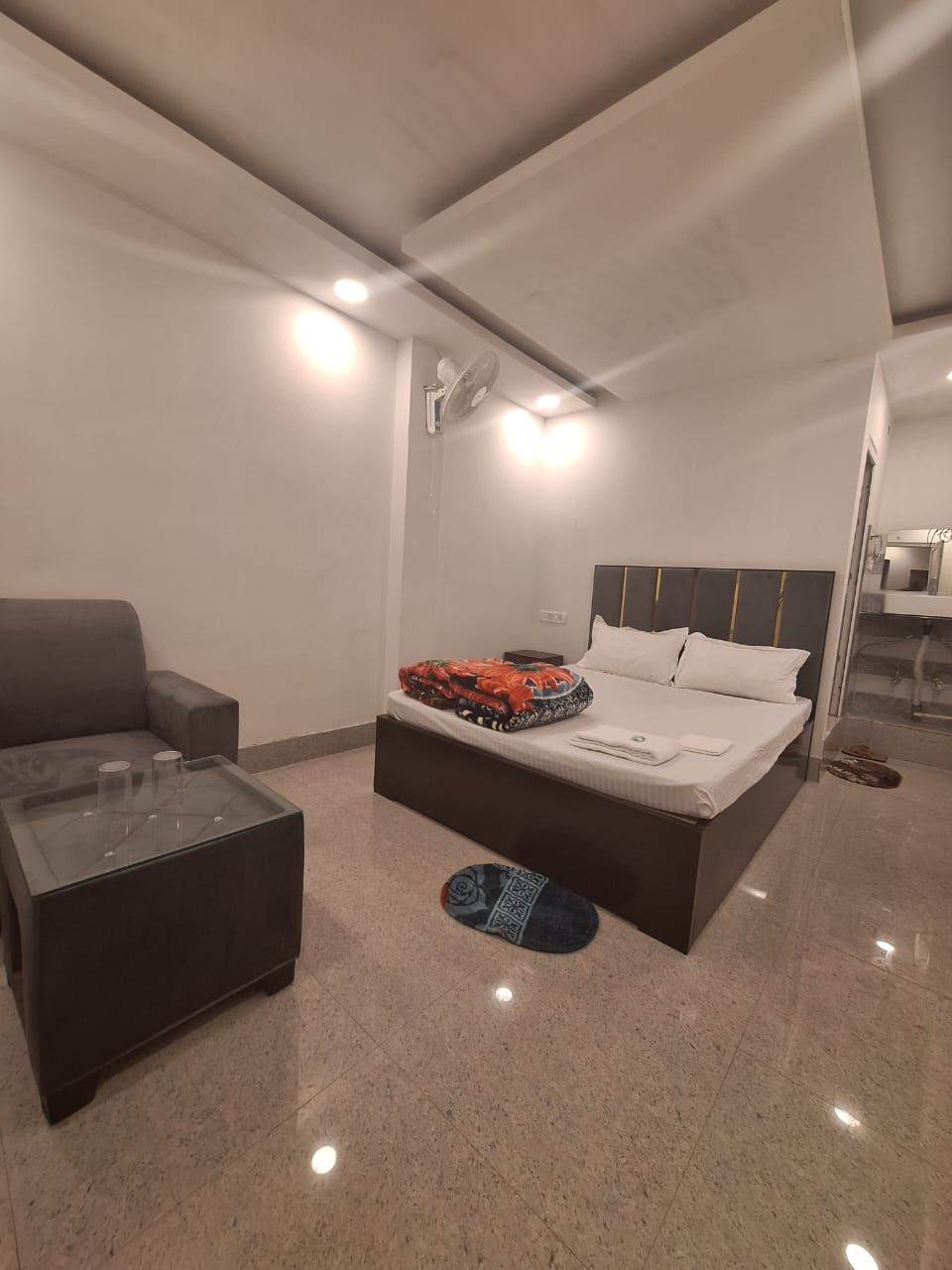 A modern bedroom with a bed, a sofa, a glass coffee table, and a small rug.