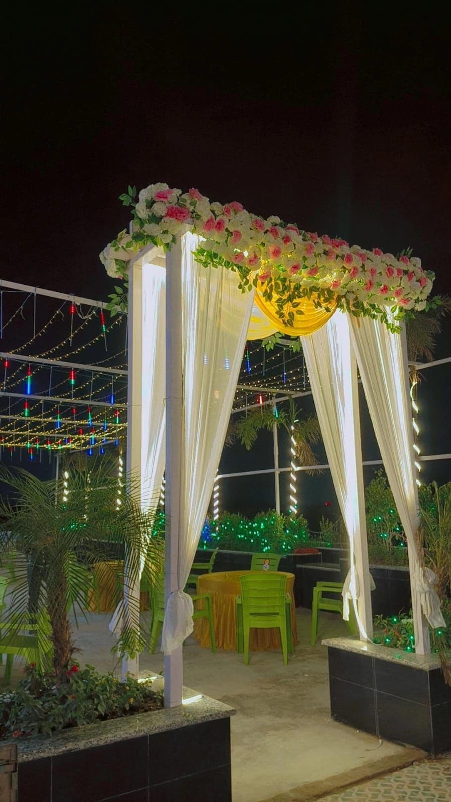 An outdoor seating area with a canopy adorned with flowers, string lights, and greenery.