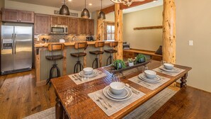 A modern kitchen with wooden cabinets, a stainless steel refrigerator, and a bar area with stools. - Walk to Ski Shuttle and Town | Hot Tub (Big Sky)