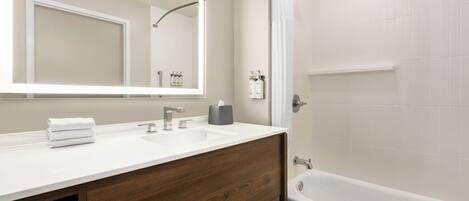 A modern bathroom with a wooden vanity, a large mirror, a bathtub, and a shower.
