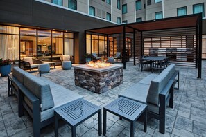 Un espace extérieur aménagé en patio, avec un foyer en pierre, des coins salon et une partie couverte comprenant des tables et des chaises.