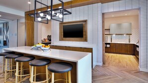 A modern kitchen with a large island, bar stools, a flat-screen TV, and a herringbone wood floor. - Staybridge Suites Grand Rapids South by IHG (Grand Rapids)
