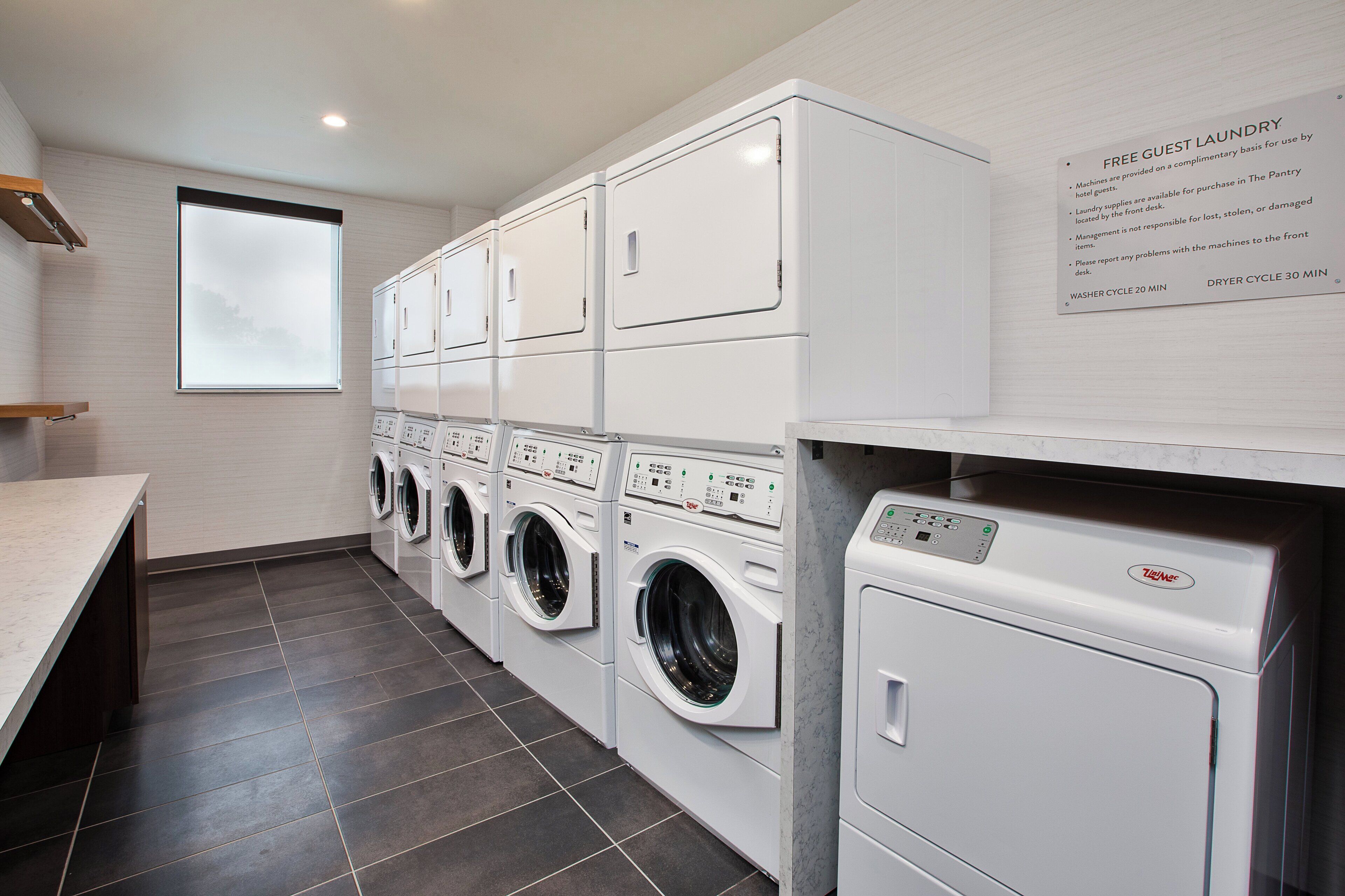 A laundry facility with multiple washing machines and dryers, a window, and a sign detailing the cycle times.