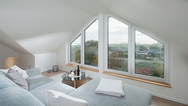 A modern living room with a high ceiling and large windows offering a view of greenery and buildings. - // APARTMENT LENE'S LOFT // (Norderney)