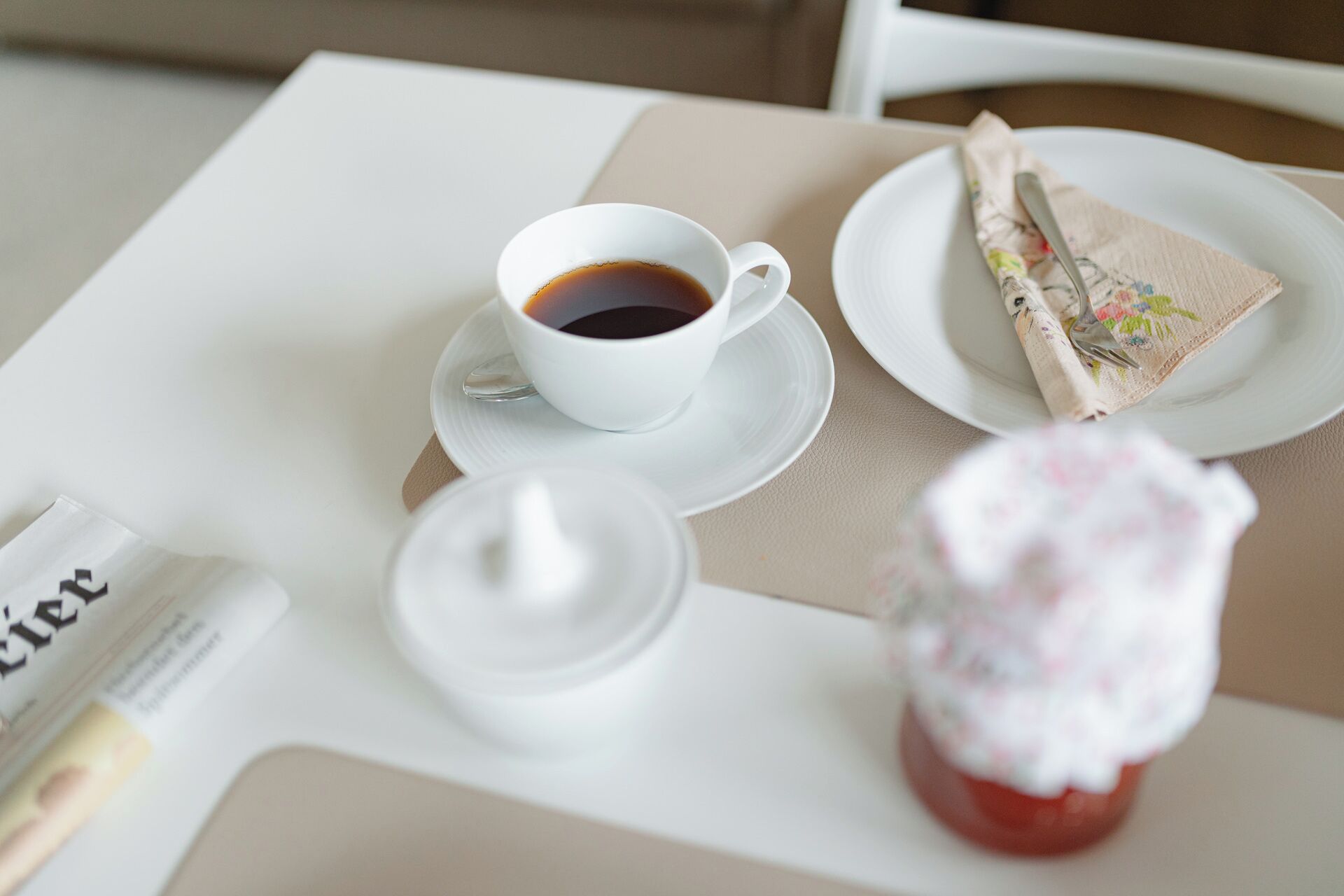 Un tavolo con una tazza di caffè, un piatto con un tovagliolo e un barattolo di marmellata.