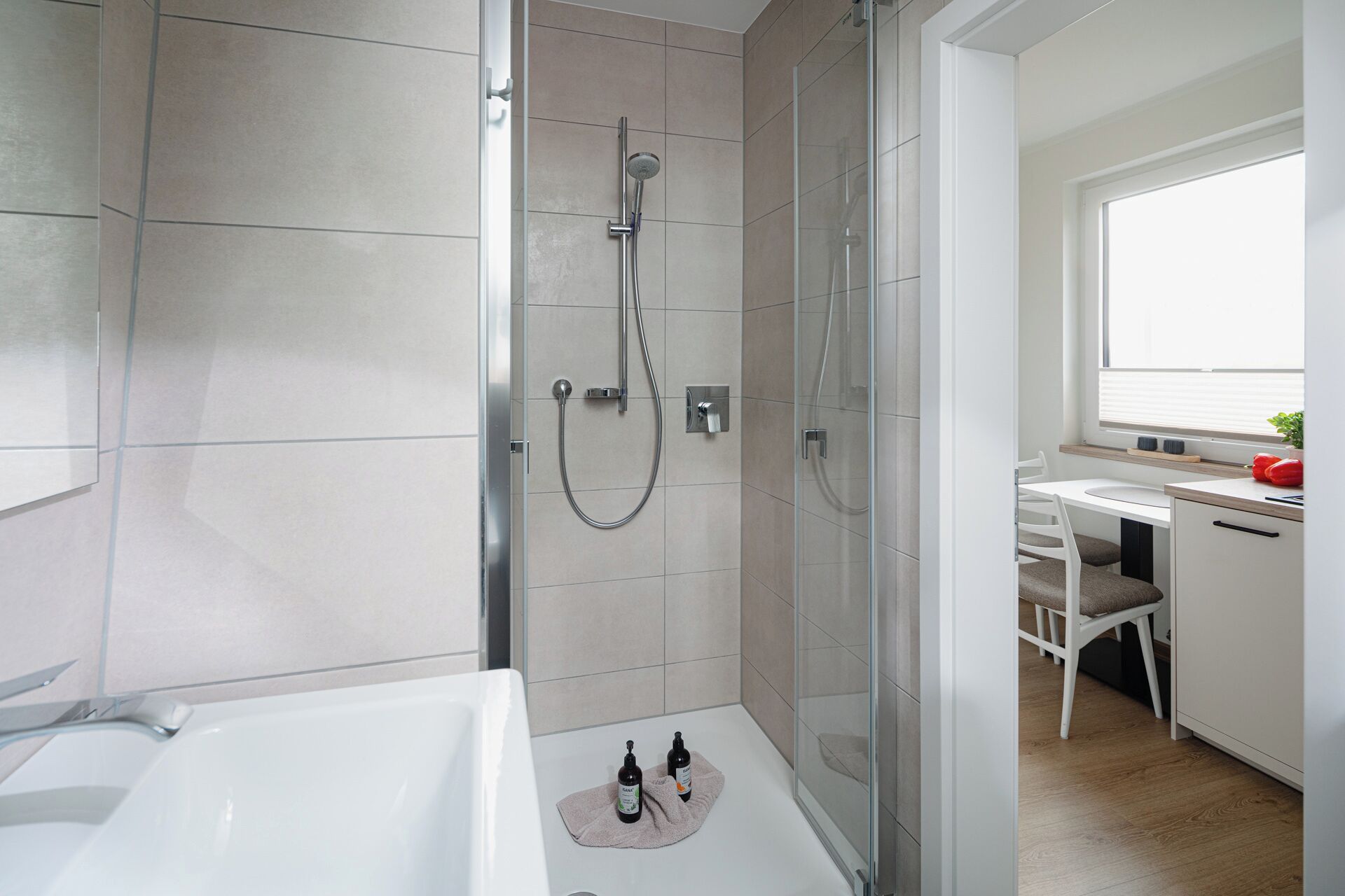Une salle de bain moderne avec une douche à parois de verre, une baignoire et un petit coin bureau avec une fenêtre.