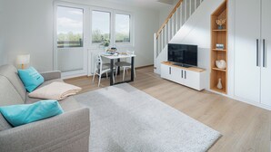 A modern living room with a sofa, a dining table, and a TV. - // APARTMENT LENE'S LOFT // (Norderney)