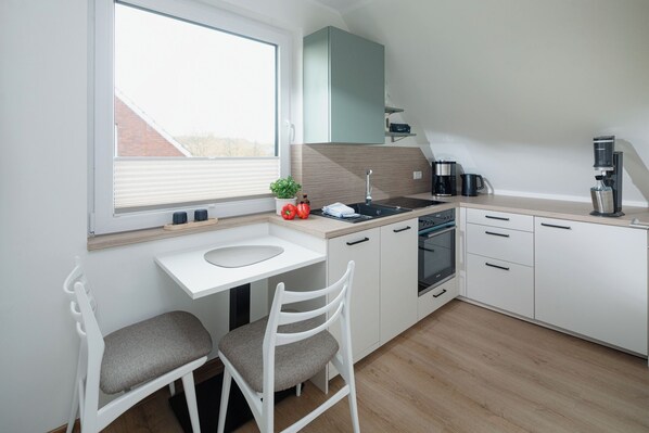 A modern kitchen with white cabinets, a built-in oven, a coffee maker, and a window overlooking a brick building.