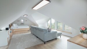 A modern loft bedroom with a bed, grey sofa, and large windows. - // APARTMENT LENE'S LOFT // (Norderney)