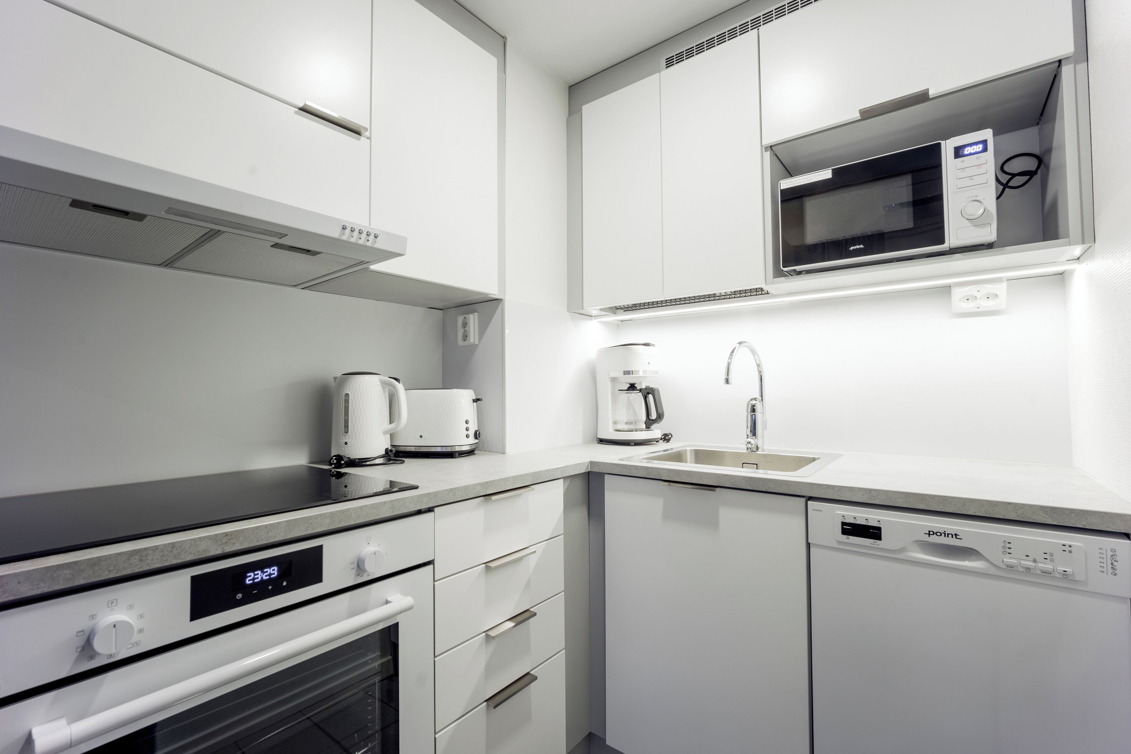 Une cuisine moderne avec des meubles blancs, un four à micro-ondes encastré, une machine à café et un lave-vaisselle.