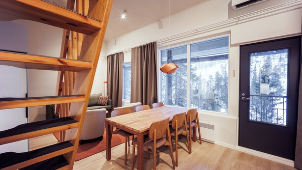A modern interior with a wooden dining table, chairs, a sofa, and a staircase. - Holiday Club Rukatunturi Apartments (Kuusamo)