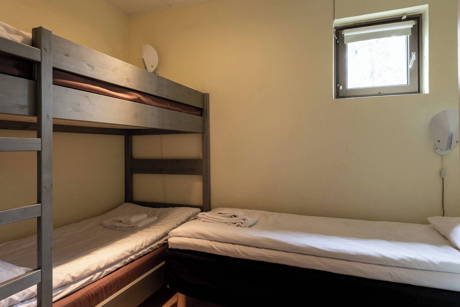 A bunk bed room with two beds, a window, and a wall-mounted light fixture.