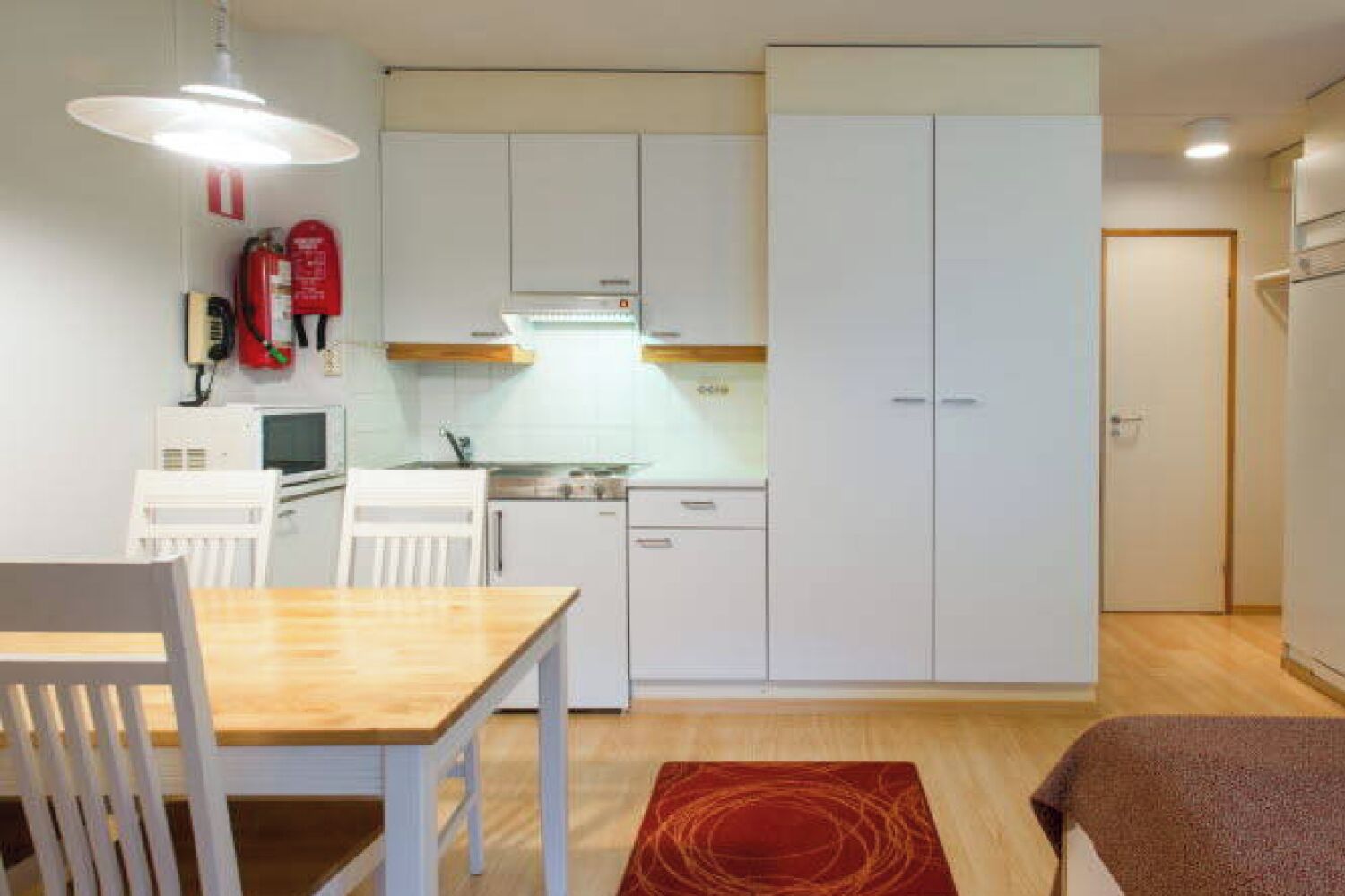 Une cuisine compacte avec des meubles blancs, un four à micro-ondes, une cuisinière et un coin repas comprenant une table et des chaises en bois.