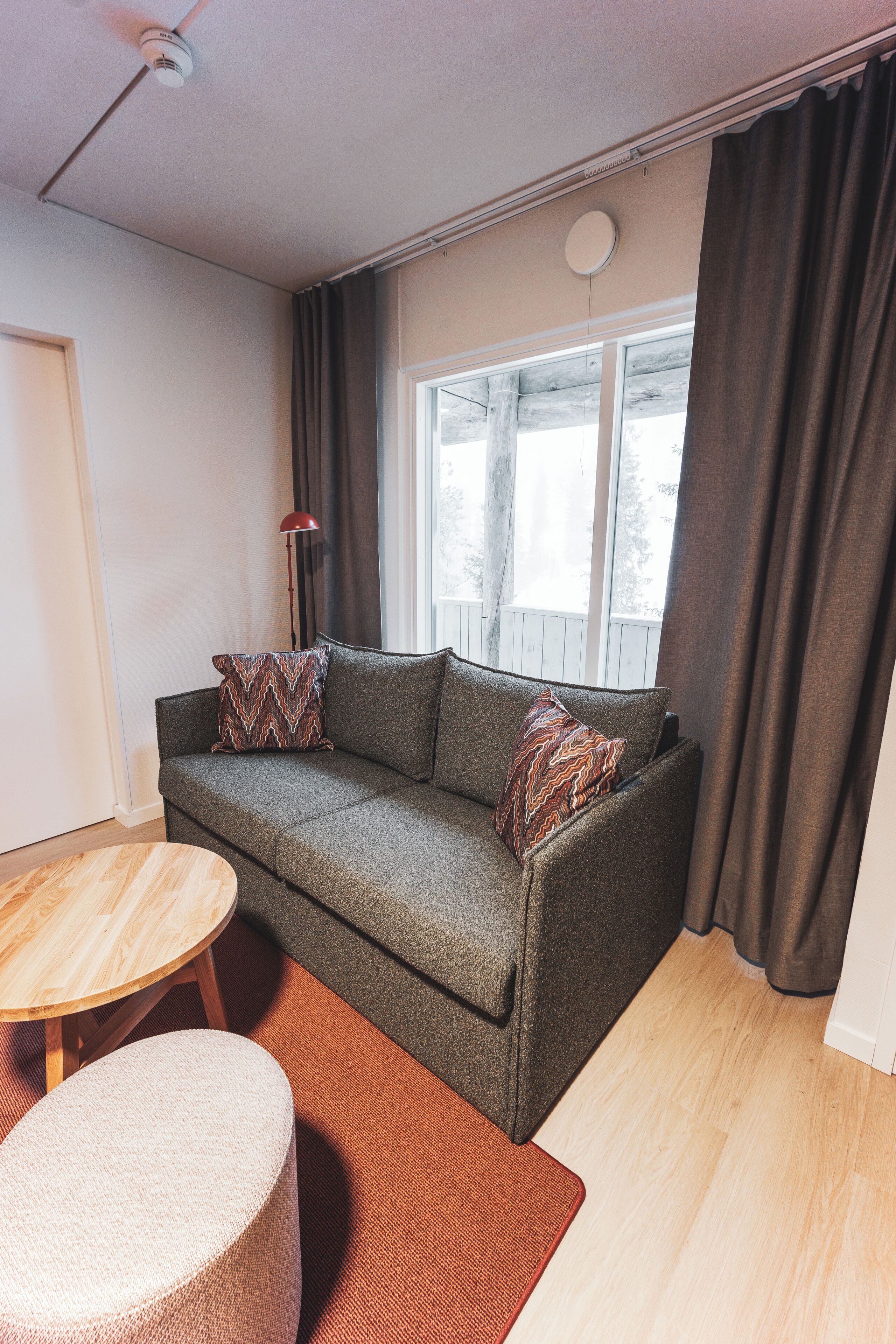 A cozy living room with a grey sofa, two patterned cushions, a small wooden table, and a round ottoman.