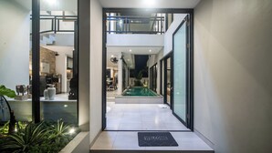 A modern interior with a glass door leading to a pool area, a welcome mat, and a staircase to an upper level. - Alsava Villa and Suites (Canggu)