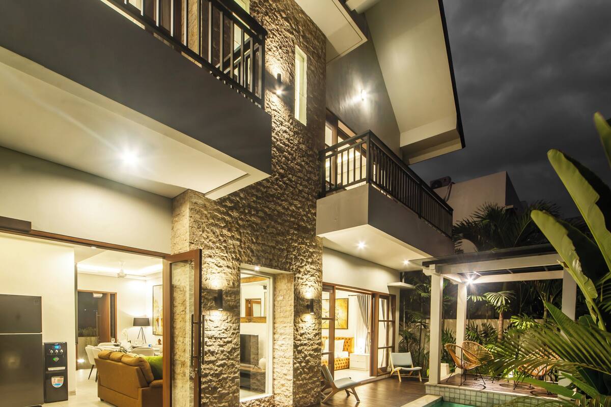 A modern two-story house with a swimming pool, a balcony, and a well-lit interior.