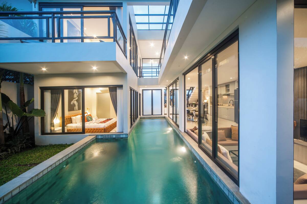 A modern house with a central swimming pool, large glass doors, and a well-lit interior.