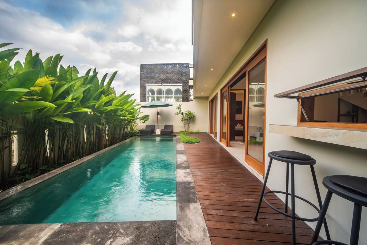 A modern outdoor pool area with a wooden deck, lounge chairs, and a bar area with stools.