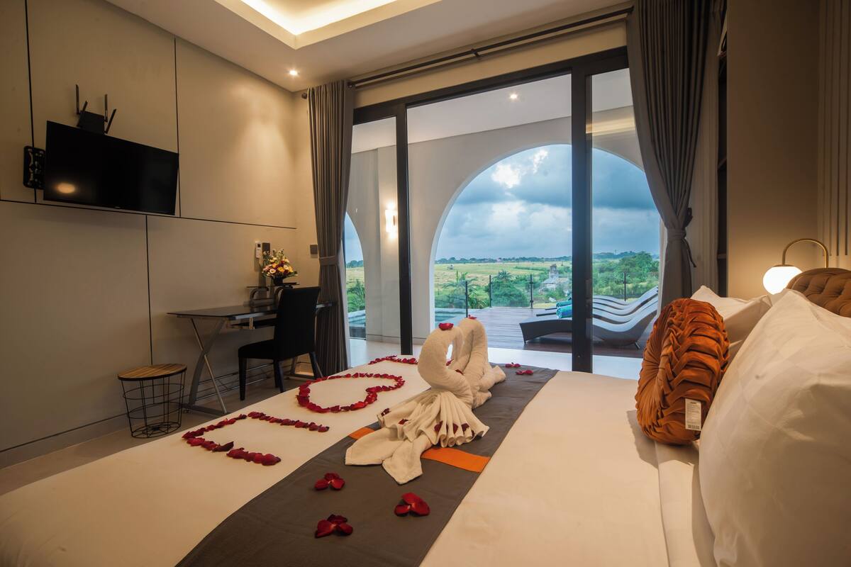 A hotel room with a bed, a desk, and a large window with a view of greenery.
