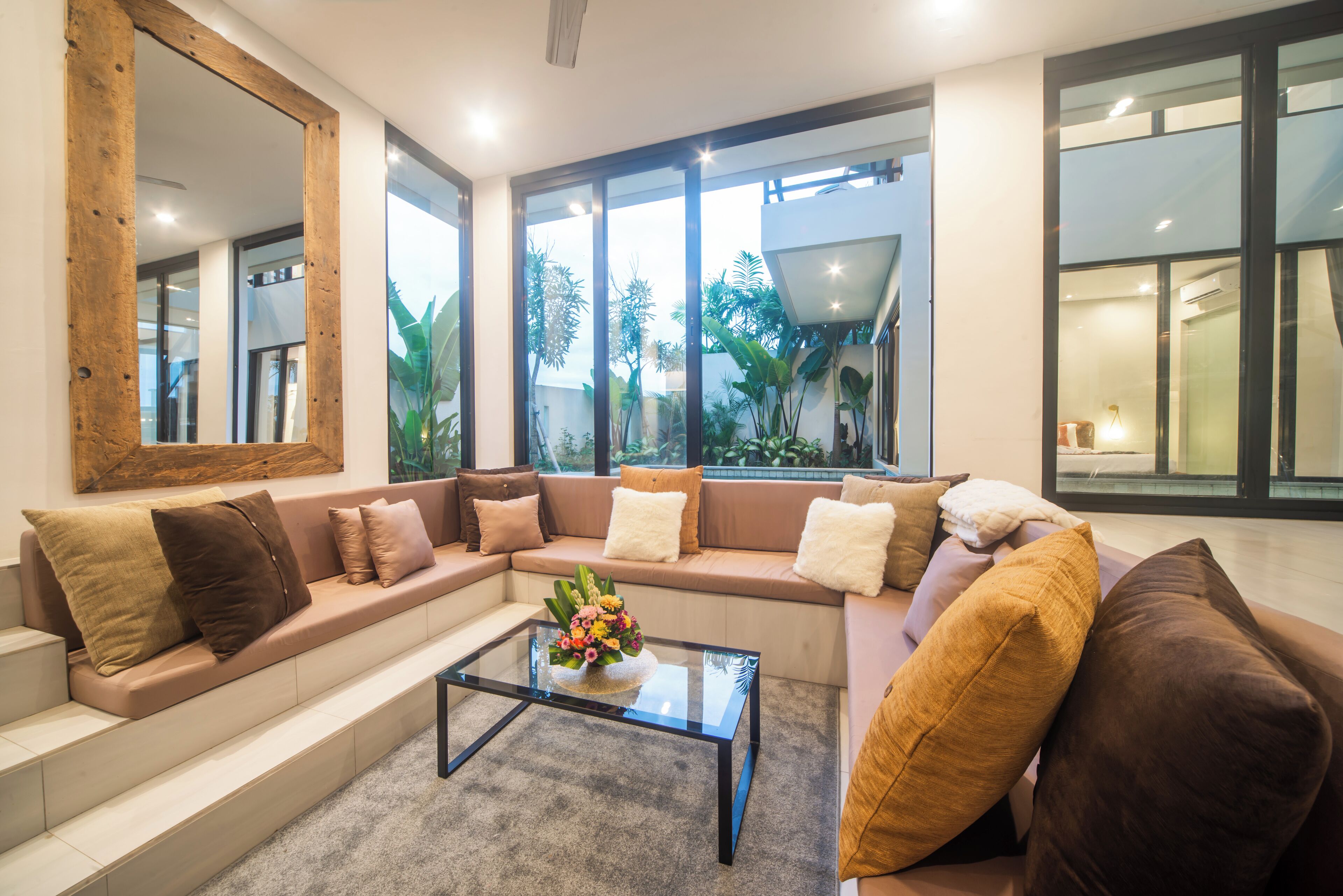 A modern living room with a beige sofa set, a glass coffee table, and a large mirror.