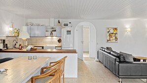Una cocina moderna con armarios blancos, una isla central y un comedor con sillas de madera.