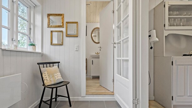 Un pasillo con una silla, una puerta que da al baño y un aparador con cristalería.