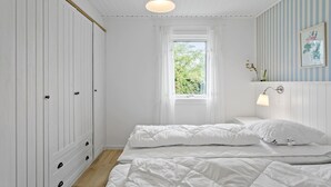 Un dormitorio con cama, armario, ventana y lámpara fijada a la pared.