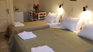 Une chambre d’hôtel avec deux lits, une petite table ornée d’un vase de fleurs et un coin cuisine.