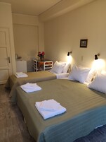 A hotel room with two beds, a small table with a vase of flowers, and a kitchenette.