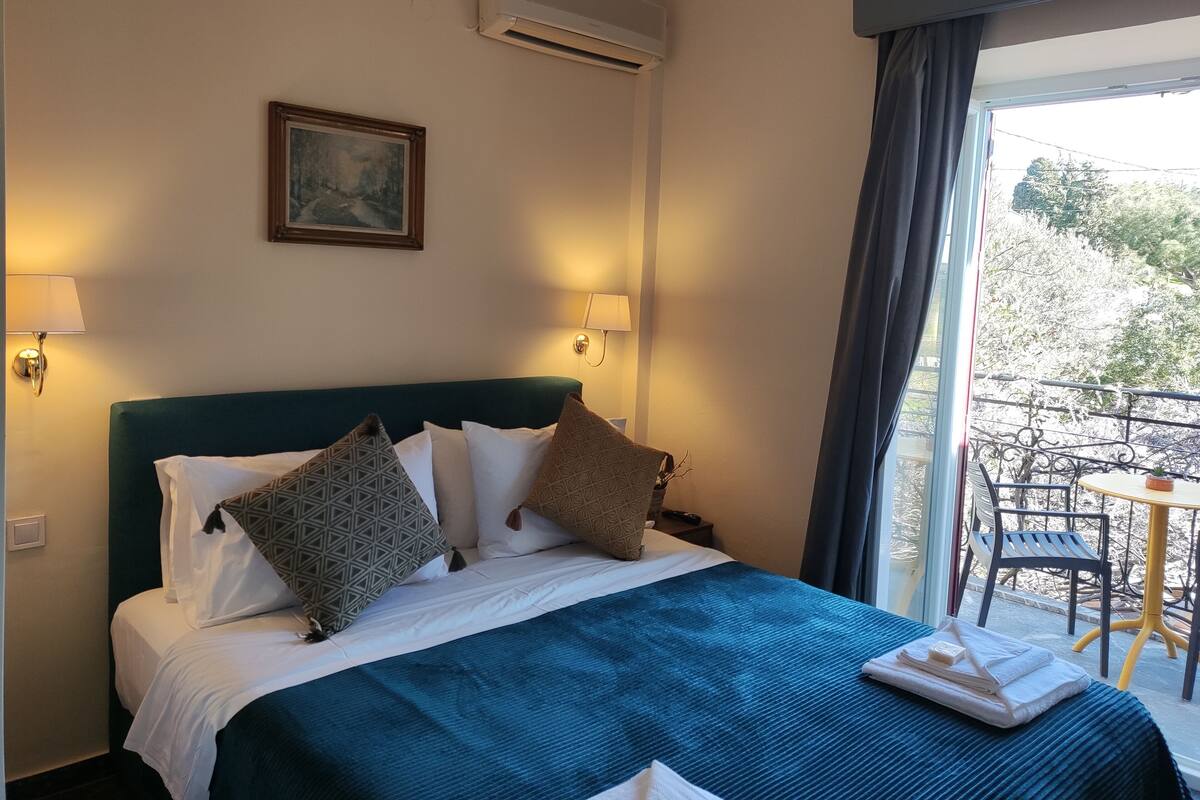 A hotel room with a bed, two wall-mounted lamps, a painting, and a view of the outdoors.
